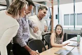 A group of coworkers standing around a laptop smiling