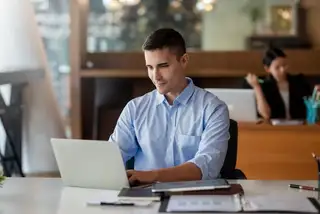 A handsome man wearing blue long sleeve working in his laptop