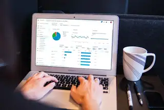 A picture of a two hands using a laptop with graphs on the screen