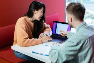 two people discussing work around a laptop