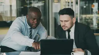 a black bald guy and a white guy wearing black tie looking at a laptop