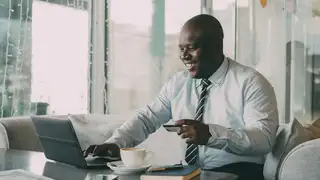 a black bald business man wearing a tie smiling while using a laptop